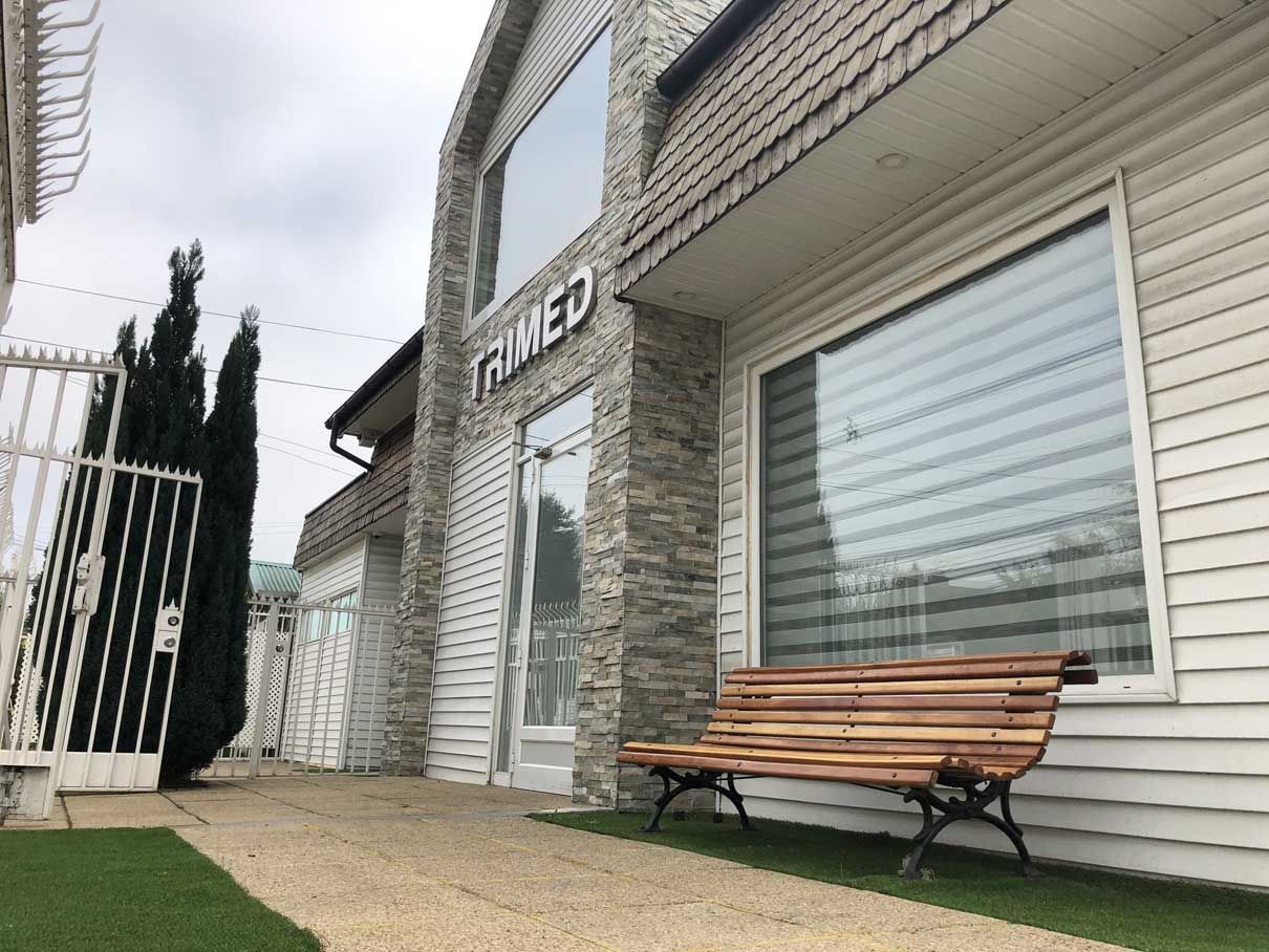 Fachada del centro TRIMED en avenida Holandesa, con revestimiento de piedra y una banca en el jardín